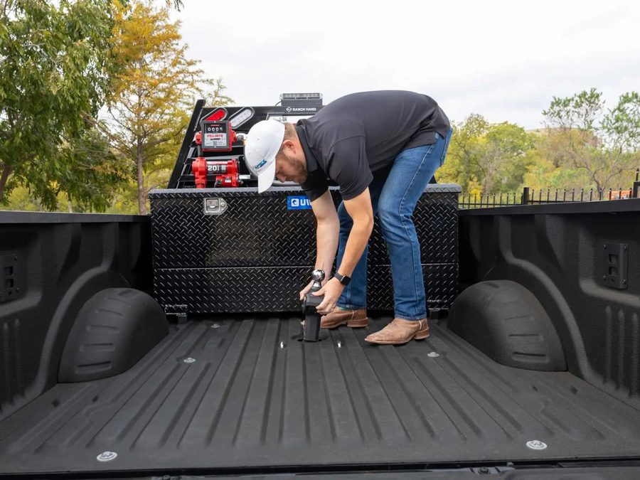 Technician installing hitch hardware in a truck bed